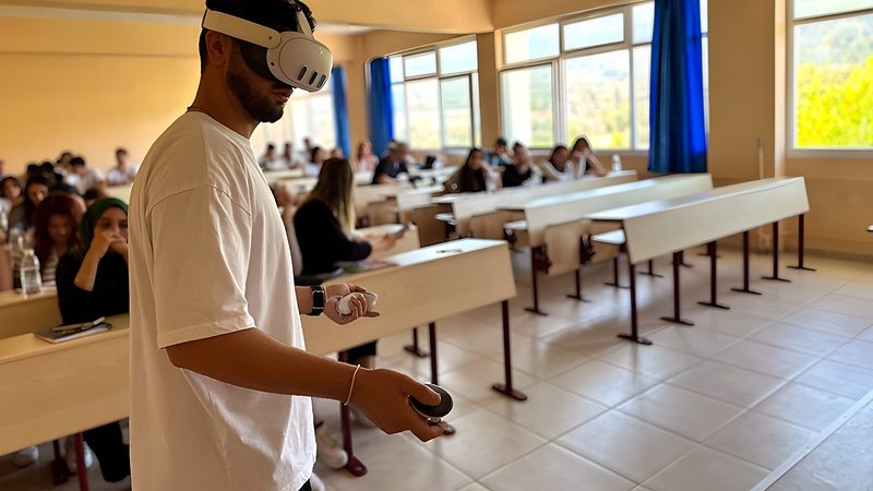 Sınıfta VR başlığıyla Imverge simülasyonunu deneyen bir İSG öğrencisi; arkada dersi izleyen öğrenciler.